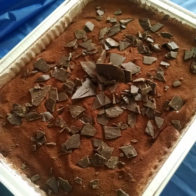 A full foil pan of homemade tiramisu, dusted with cocoa and topped with dark chocolate shards