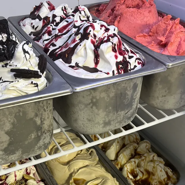Steel pans of gelato on freezer shelves, swirled with fudge and caramel
