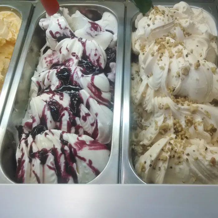 Pans of gelato close up: a blueberry swirl beside a white gelato scattered with nuts