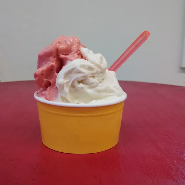 Pink and white gelato in a yellow cup with a pink spoon, on a red table