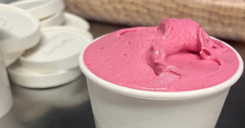 A take-home cup heaped with bright pink gelato, a stack of lids beside it