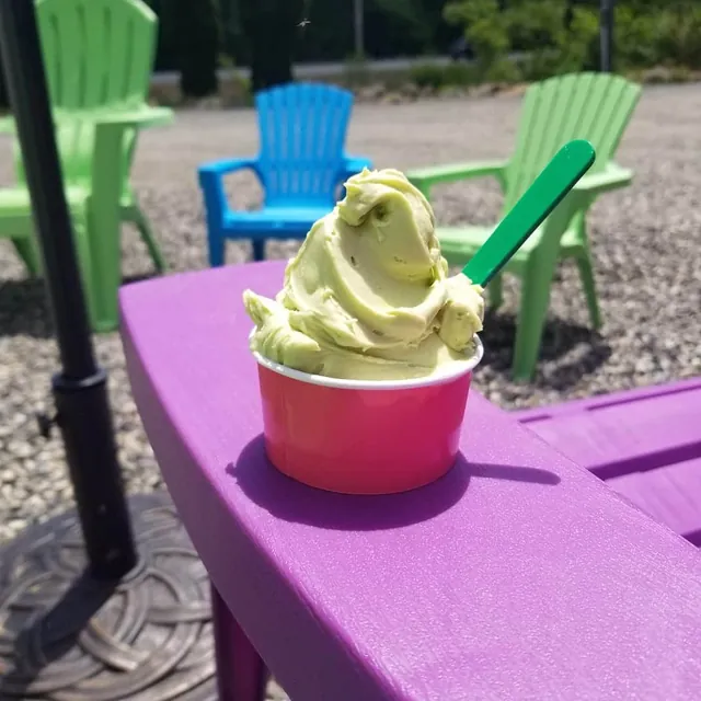 Pale green gelato heaped in a pink cup on a purple patio table
