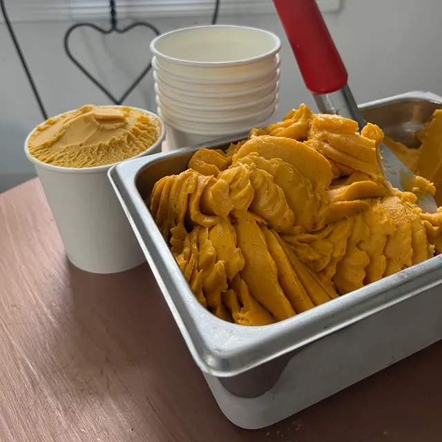 Orange pumpkin sorbetto in a steel pan beside a filled take-home cup