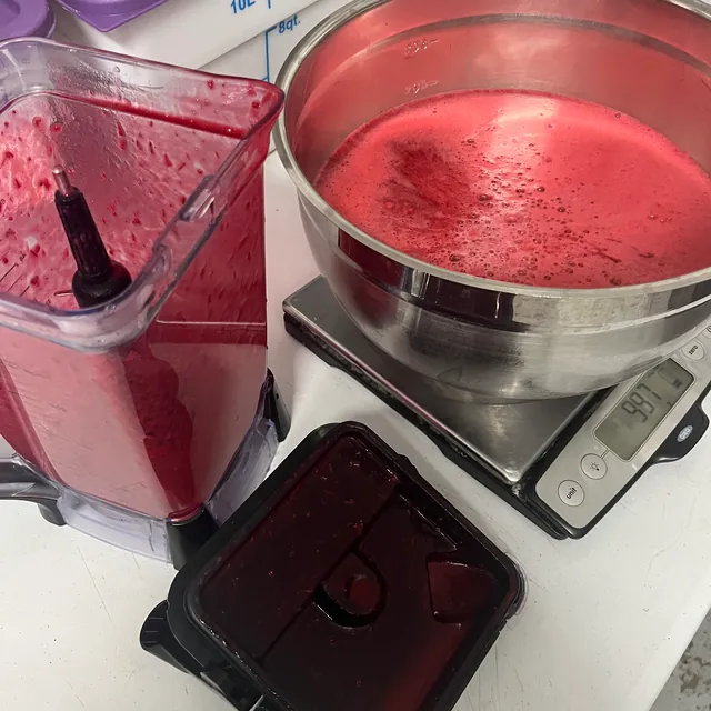 Fresh red fruit purée in a blender jug and a steel bowl on a kitchen scale