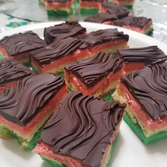 Squares of Italian rainbow cookie, green, white and pink layers under wavy dark chocolate