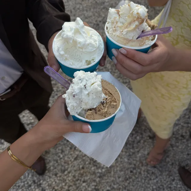 Three guests holding blue cups of gelato together over a gravel drive
